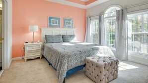 A bedroom with a bed, nightstand, lamp, and ottoman. - Pool Access + Balcony: Barefoot Resort Retreat! (North Myrtle Beach)