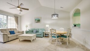 A living room with a ceiling fan, a dining table with chairs, a sofa, and a window with curtains. - Pool Access + Balcony: Barefoot Resort Retreat! (North Myrtle Beach)