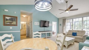 A living room with a round wooden table, white chairs, a beige sofa, and a television. - Pool Access + Balcony: Barefoot Resort Retreat! (North Myrtle Beach)