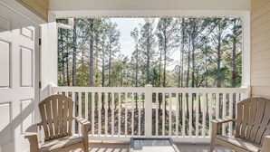 A porch with two Adirondack chairs and a glass-top table, overlooking a forested area. - Pool Access + Balcony: Barefoot Resort Retreat! (North Myrtle Beach)