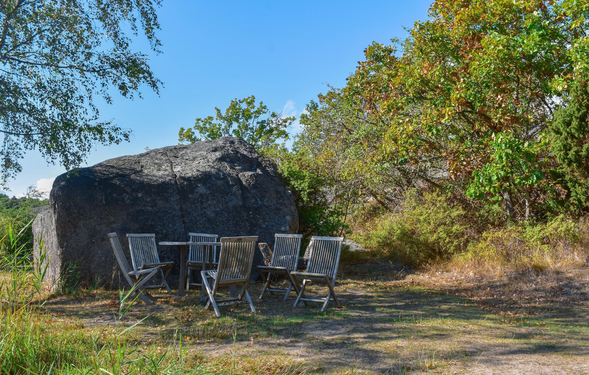 Een natuurlijke omgeving met een grote rots, een tafel en vier stoelen.