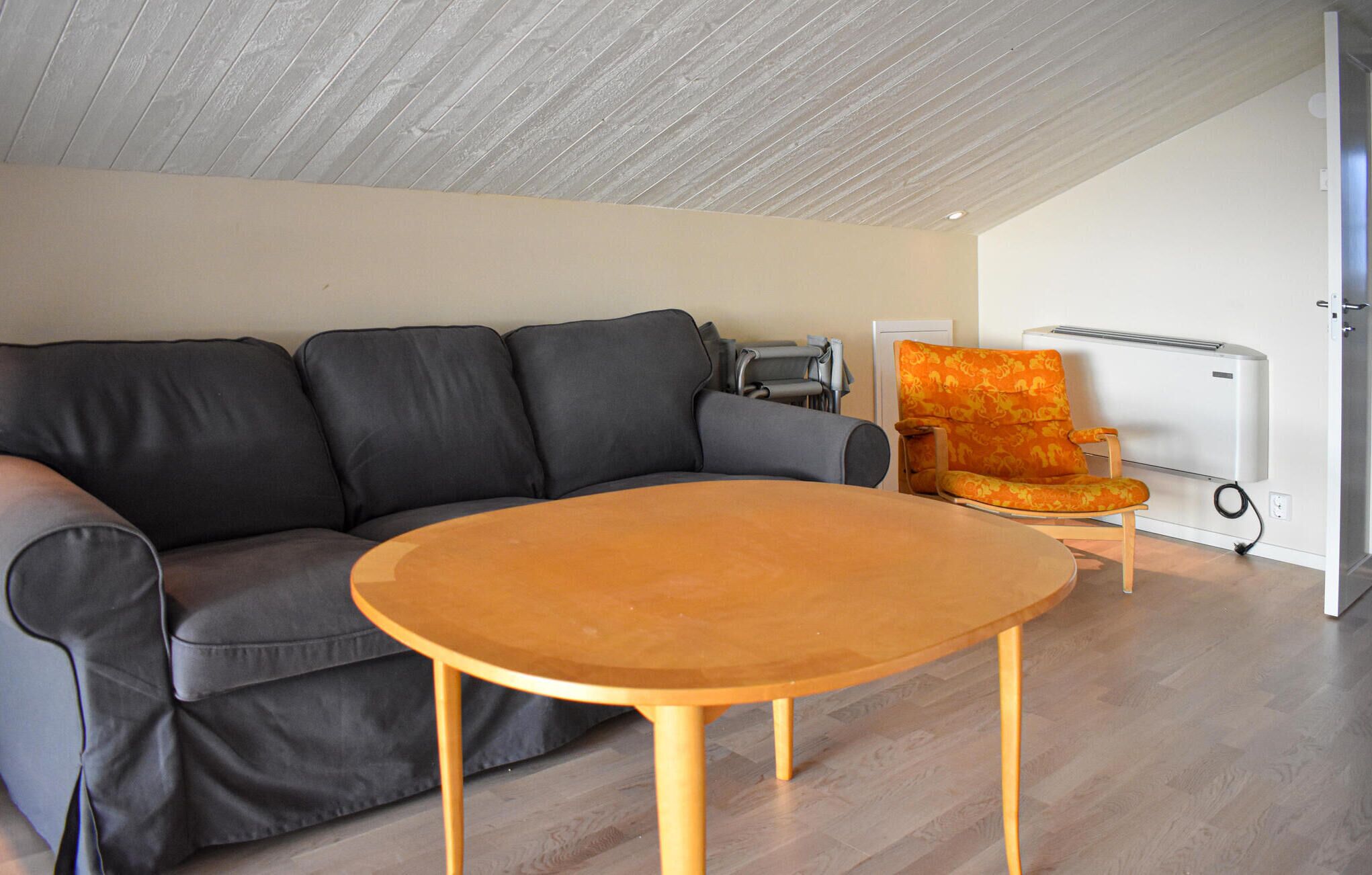 Una sala de estar con un sofá gris, una mesa de centro de madera y un sillón naranja estampado.