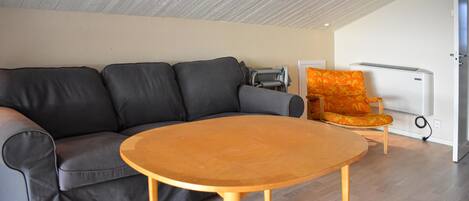 Una sala de estar con un sofá gris, una mesa de centro de madera y un sillón naranja estampado.