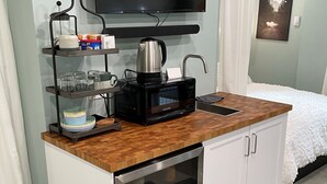 A compact kitchenette with a microwave, kettle, and coffee maker on a wooden countertop, a small sink, and a glass-fronted storage unit. - West Seattle Hideaway, 5 min from downtown/stadiums (Seattle)