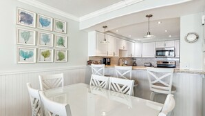 Une cuisine moderne avec des meubles blancs, un îlot central doté de sièges et un coin repas avec une table en verre et des chaises blanches.