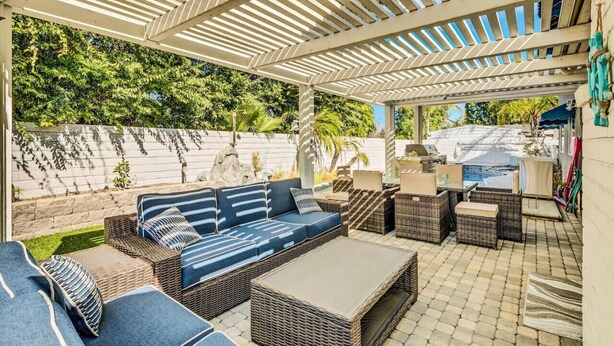An outdoor patio area with wicker furniture, a covered seating area, and a view of a backyard.