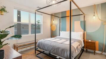 Un dormitorio moderno con cama con dosel, una mesita de noche, un banco y un ventanal grande.