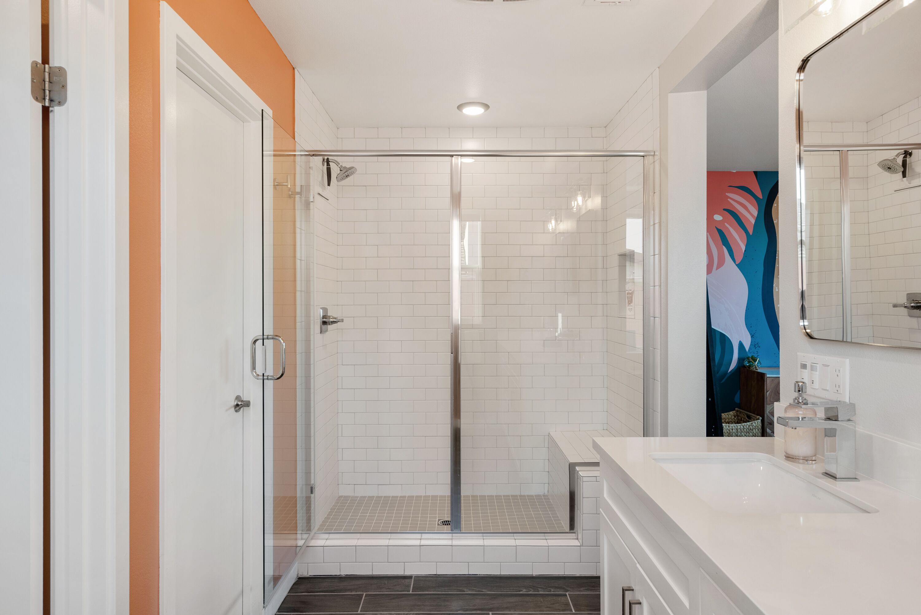 Un baño moderno con ducha envuelta en vidrio, azulejos blancos y un lavamanos blanco con espejo.