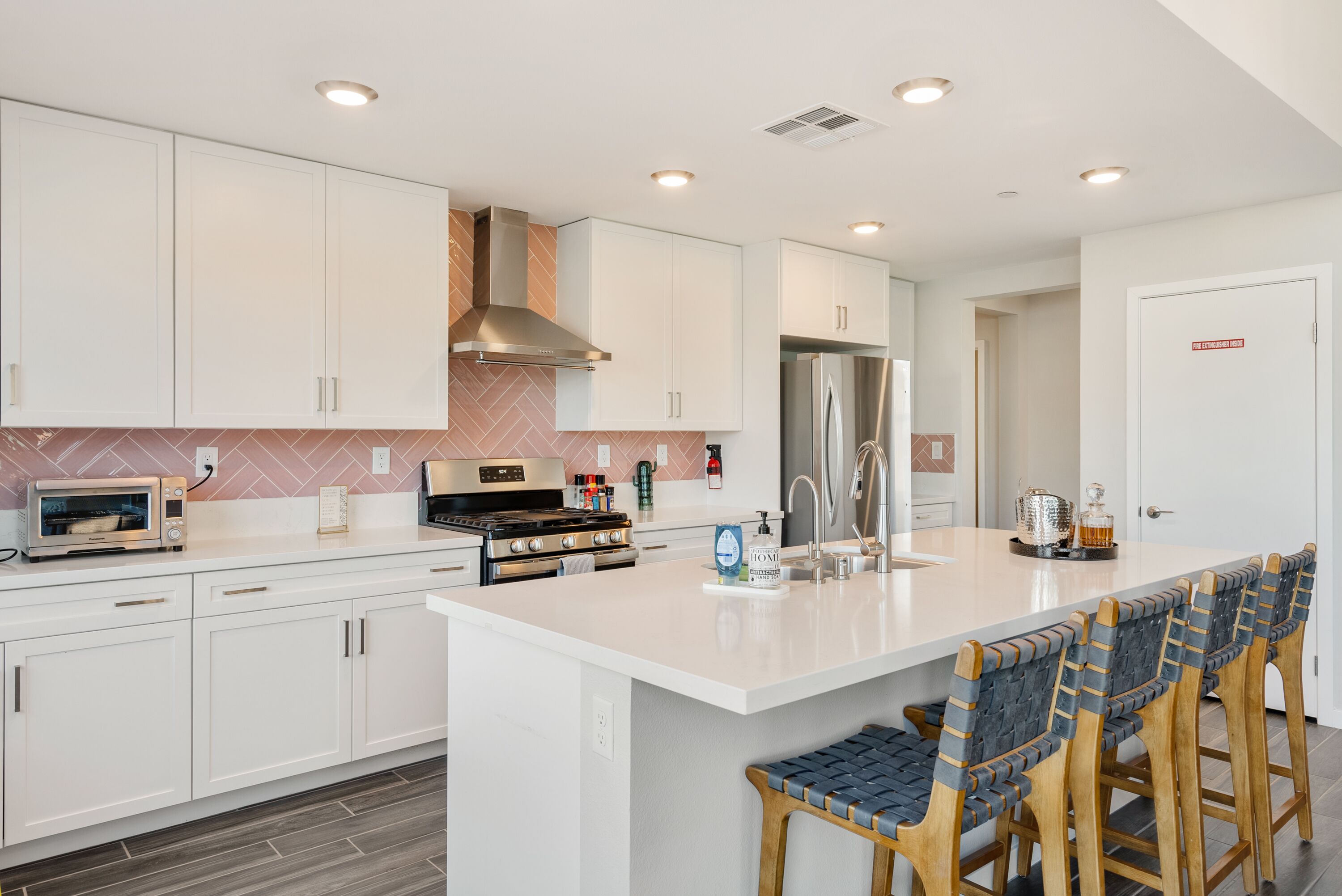 A modern kitchen with white cabinets, a stainless steel refrigerator, a built-in oven, and a large island with bar stools.