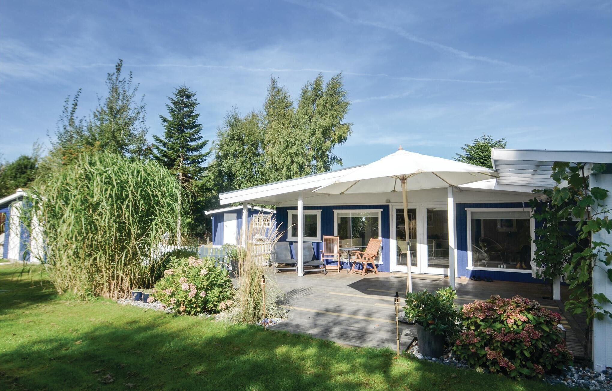 Eine überdachte Terrasse mit Gartenmöbeln, ein kleiner Gartenbereich und ein Gebäude mit blauer Fassade.