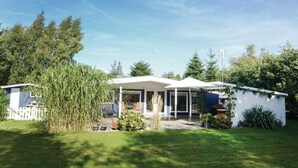 Ein eingeschossiges Haus mit überdachter Terrasse, umgeben von einem gepflegten Rasen und verschiedenen Pflanzen.