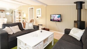 Ein gemütliches Wohnzimmer mit einem weißen Couchtisch, zwei dunklen Sofas, einem Fernseher und einem Kaminofen.