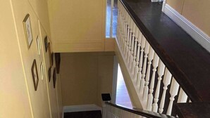 Una scala con finitura in legno scuro e balaustre bianche, che conduce a un pianerottolo al secondo piano con un piano di lavoro nero e una sedia.