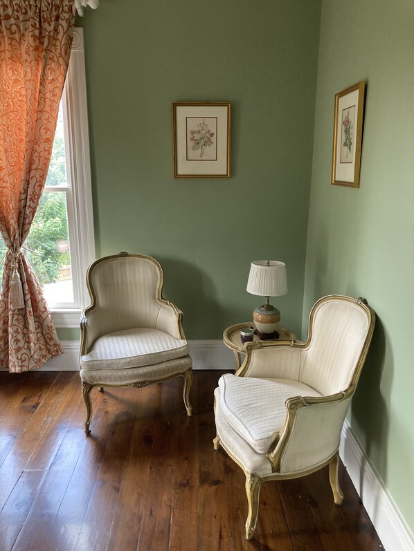 Una habitación con dos sillones decorados, una mesita con una lámpara y dos cuadros con motivos florales en la pared.