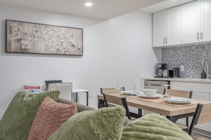 A modern kitchen with white cabinets, a black tiled backsplash, and a dining area with a wooden table set for two.