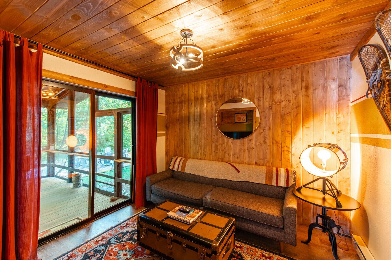 A cozy room with a wooden ceiling, a sofa, a small table with a lamp, and a window with curtains.