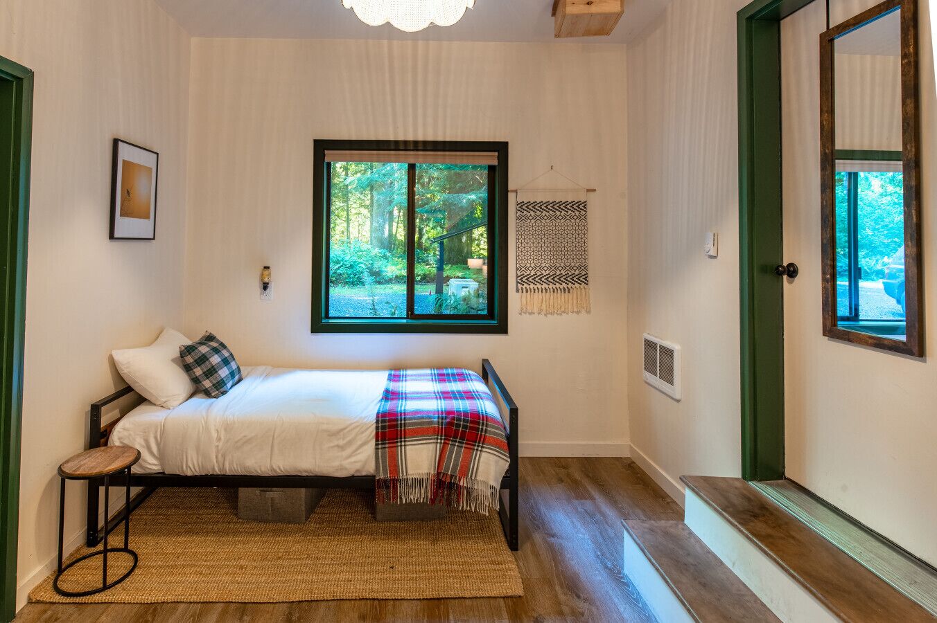 Een slaapkamer met een bed, een raam met uitzicht op groen, wandtapijt en een deur met groene omlijsting.