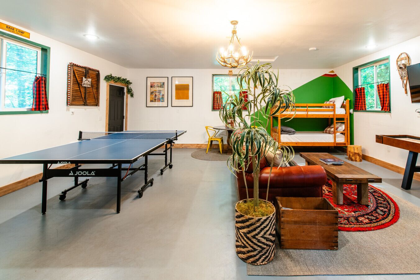 Een kamer met een tafeltennistafel, stapelbedden, een plant en een houten tafel.