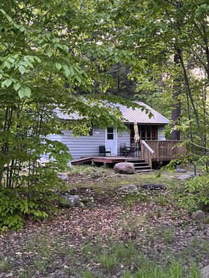 A cabin with a porch, surrounded by trees and a grassy area with rocks. - Two Cottages-On Island- Great for two families (Archipelago)