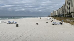 Uma praia com fileiras de cadeiras e guarda-sóis de praia, uma placa de proibido a entrada de pessoas não autorizadas e uma linha de edifícios altos ao fundo.