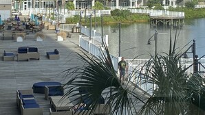 Um hotel alto com várias varandas, um calçadão à beira-mar com assentos e um píer que se estende sobre a água.