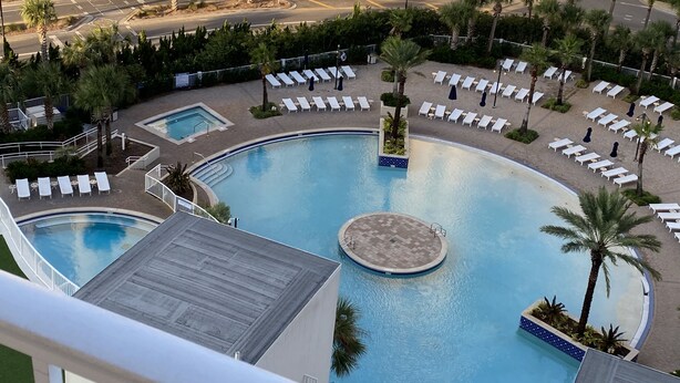Área de piscina de hotel com vários espaços para banho de sol e uma fonte central.
