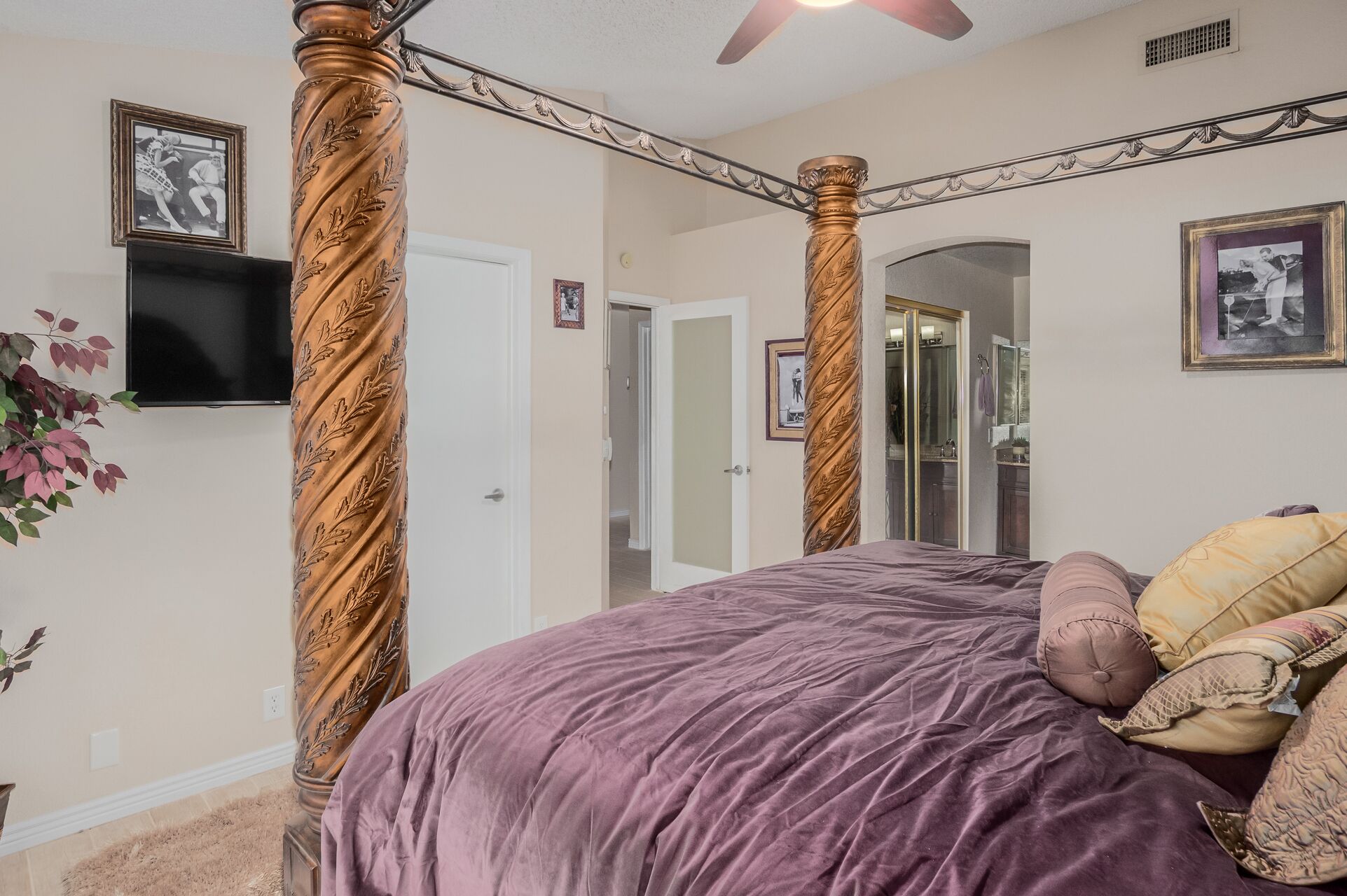 A bedroom with a four-poster bed, a television mounted on the wall, and a door leading to another room.