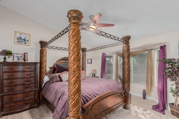 A four-poster bed with a ceiling fan, a dresser with multiple drawers, and a potted plant.