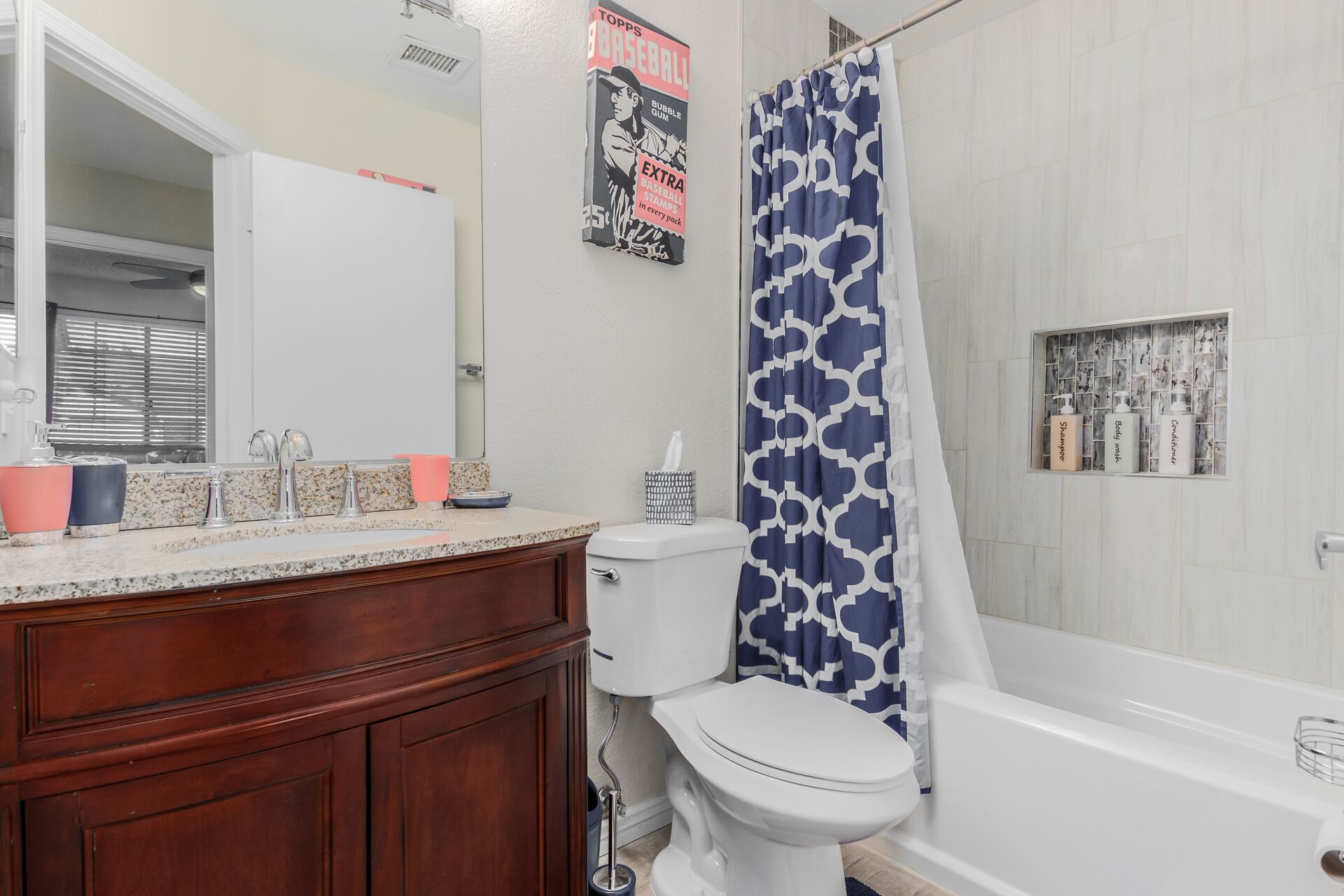 Une salle de bain avec des toilettes blanches, un lavabo avec un miroir, un rideau de douche et des articles de toilette accrochés au mur.