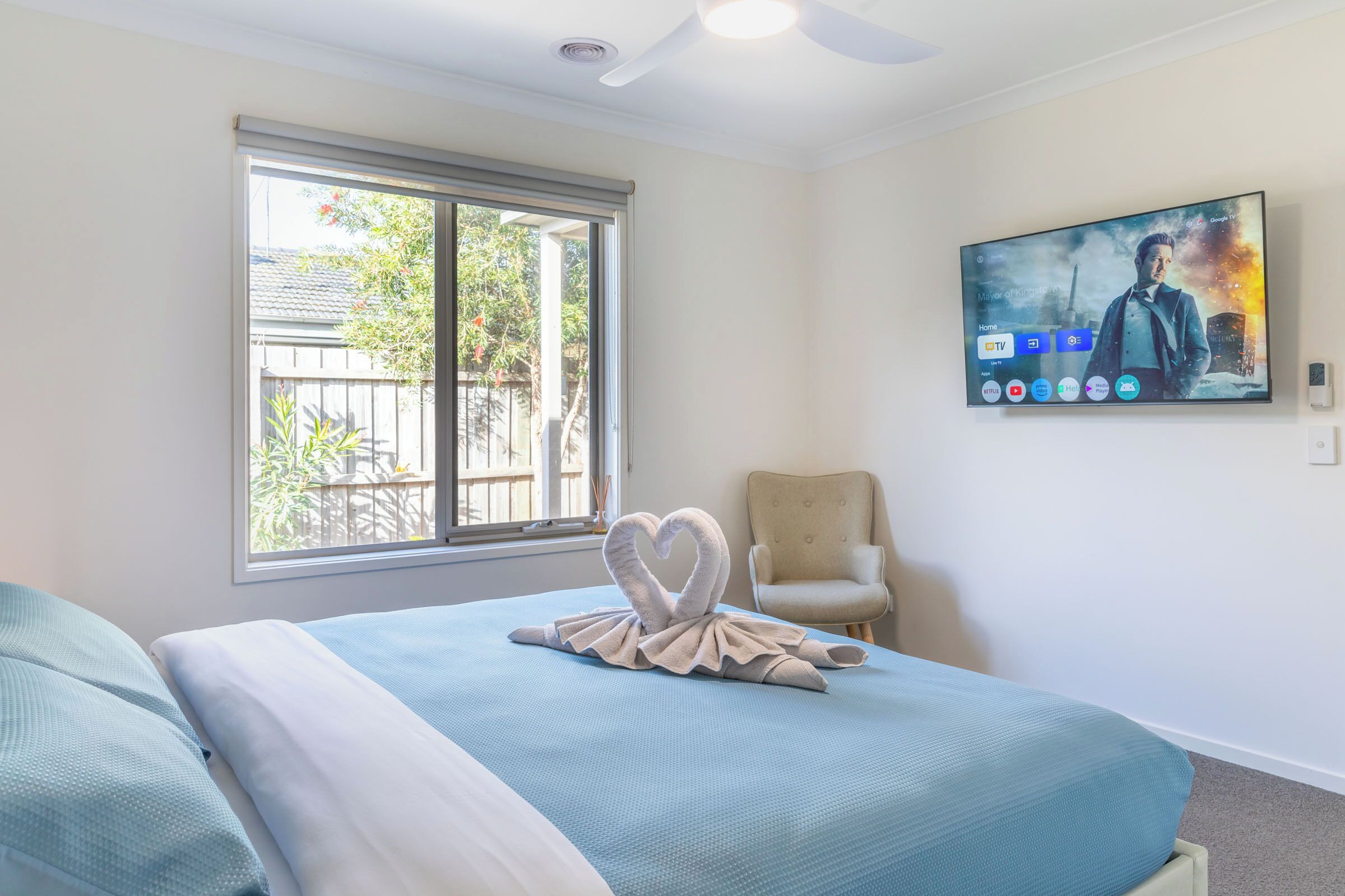 A hotel room with a bed, a chair, a TV on the wall, and a window with a view of the outside.