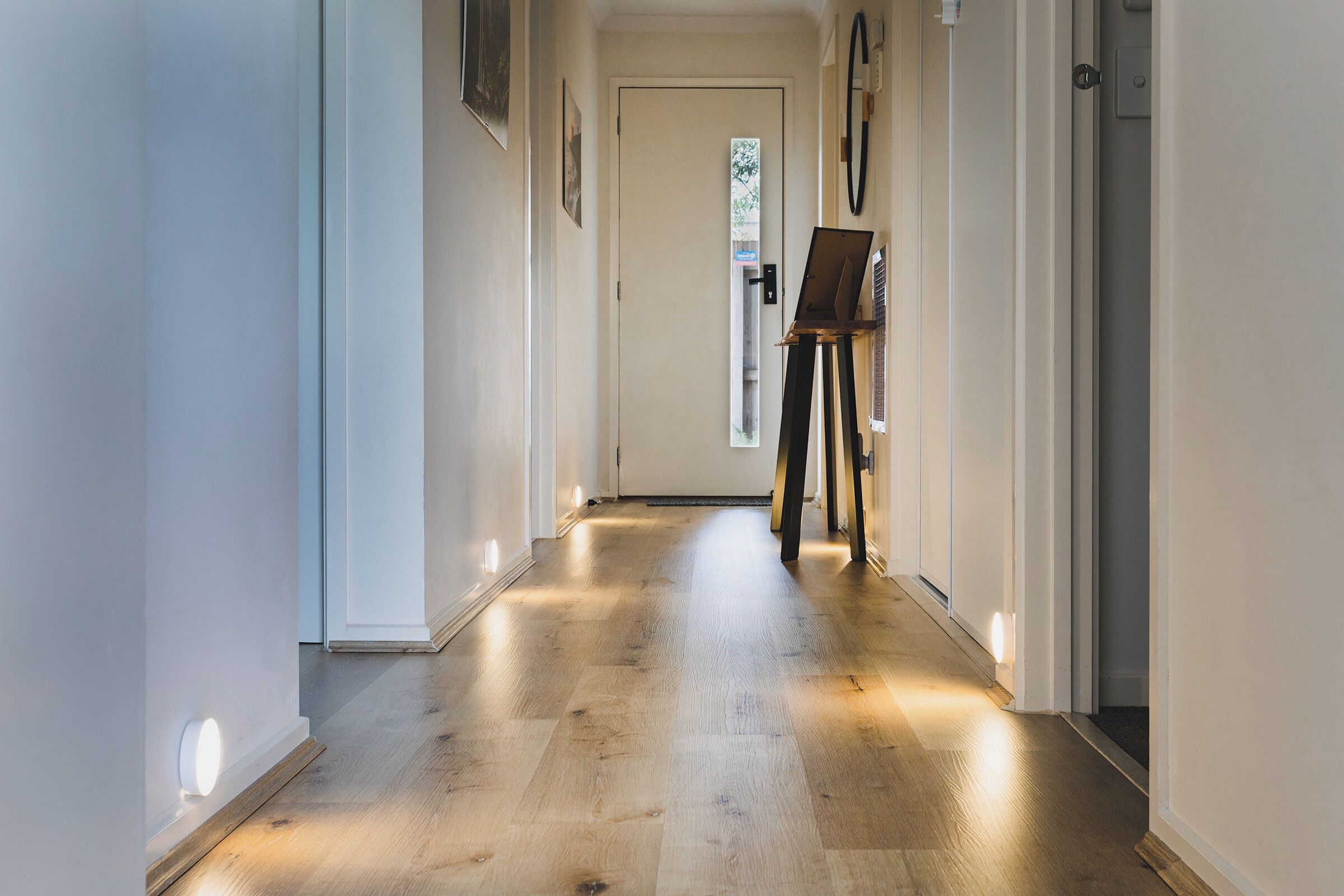 A hallway with a wooden floor, a door at the end, and an easel with a painting.