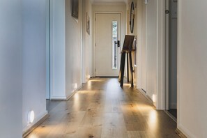 A hallway with a wooden floor, a door at the end, and an easel with a painting.
