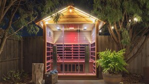 Una estructura de madera con puerta de cristal, un banco de madera y una planta en maceta.