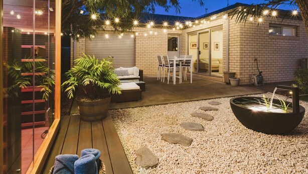 Un patio bien iluminado con una zona de estar, una fuente de agua y luces colgantes.
