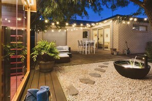 Un patio bien iluminado con una zona de estar, una fuente de agua y luces colgantes.