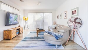 Una sala de estar moderna con televisor, mueble de madera, sofá, mesa de centro y ventilador.