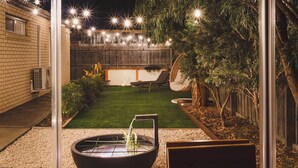 Un patio trasero con un brasero, césped, una silla colgante y una valla de madera.