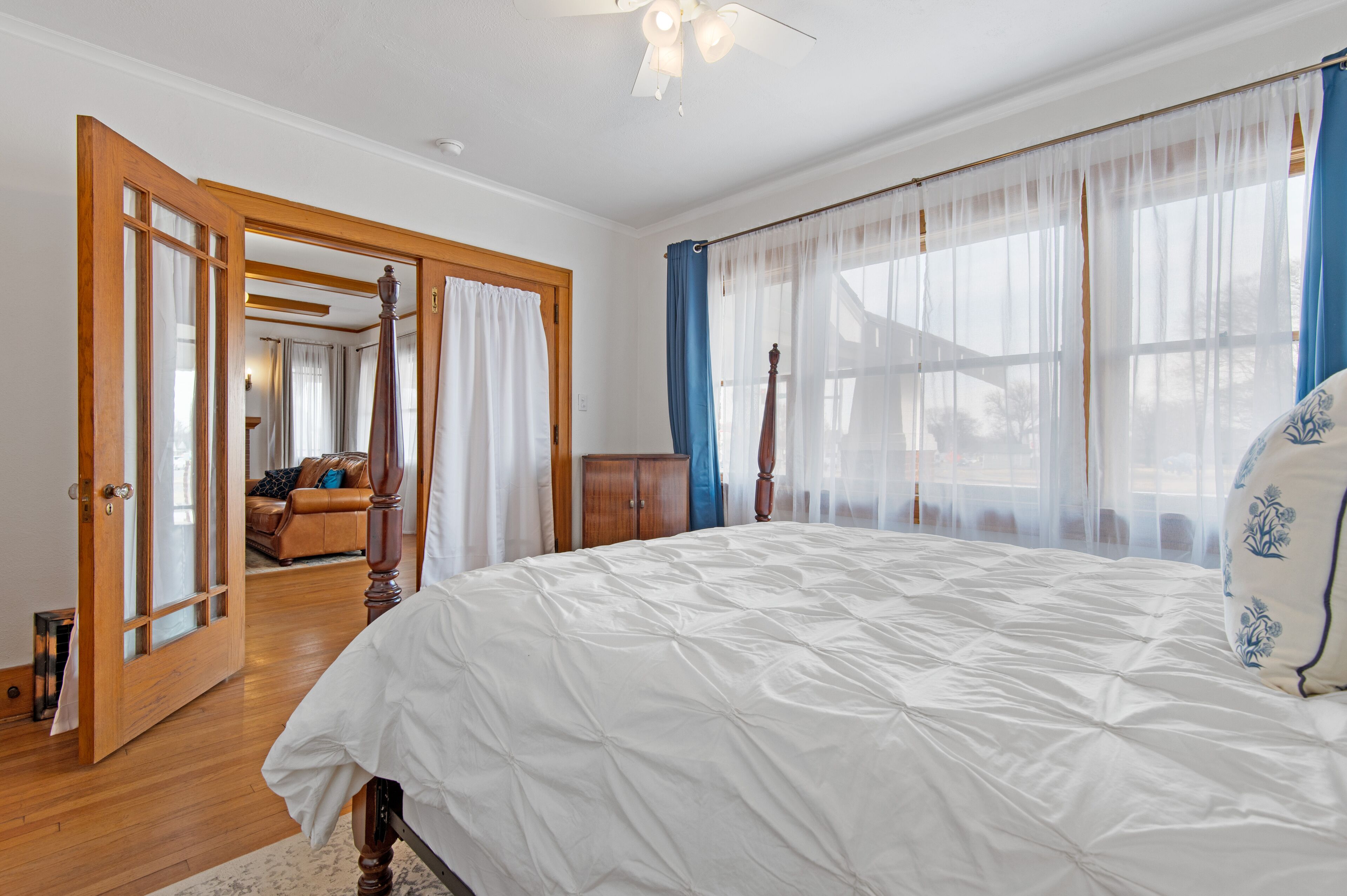 Un dormitorio amplio con una cama grande, piso de madera y vistas al exterior a través de cortinas translúcidas.