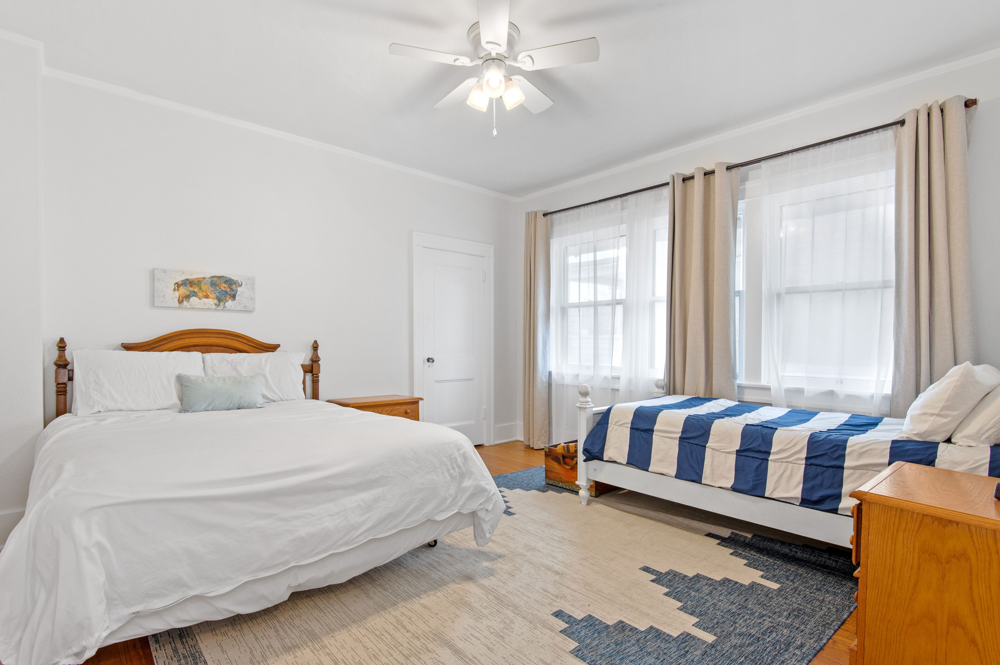 A bedroom with a large bed, a smaller bed, a ceiling fan, and a window with curtains.