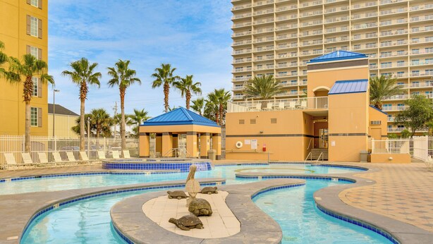 Ein Schwimmbecken mit einer Schildkrötenstatue, Palmen und einem Hotel im Hintergrund.