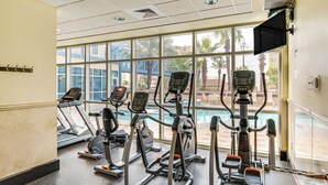 Ein Fitnessstudio mit Laufbändern, Crosstrainern und einem Poolbereich, der durch große Fenster sichtbar ist.