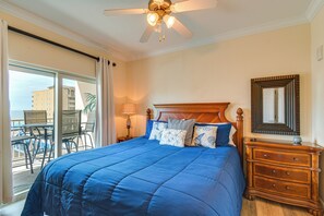 Un dormitorio con una cama grande, cabecera de madera, mesita de noche, cómoda, ventilador de techo y vistas a un balcón con mobiliario exterior.