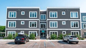 A multi-story building with a modern design, featuring a central entrance and parking spaces in front. - 2BR Condo + Shared Rooftop + Dogs Allowed (Traverse City)