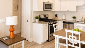 A modern kitchen with white cabinetry, a built-in microwave, a stove, and a dining area with a table and chairs. - 2BR Condo + Shared Rooftop + Dogs Allowed (Traverse City)