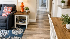 A hallway with a sofa, a small table with a lamp, a rug, and a kitchen area with cabinets and a countertop. - 2BR Condo + Shared Rooftop + Dogs Allowed (Traverse City)