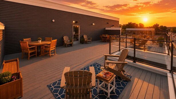 A deck with wooden furniture, a glass railing, and a sunset view. - 2BR Condo + Shared Rooftop + Dogs Allowed (Traverse City)
