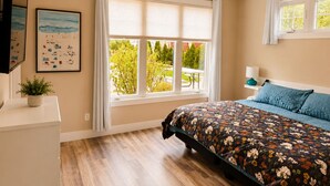 A bedroom with a bed, a ceiling fan, a window with blinds, a plant, and a framed picture on the wall. - 2BR Condo + Shared Rooftop + Dogs Allowed (Traverse City)