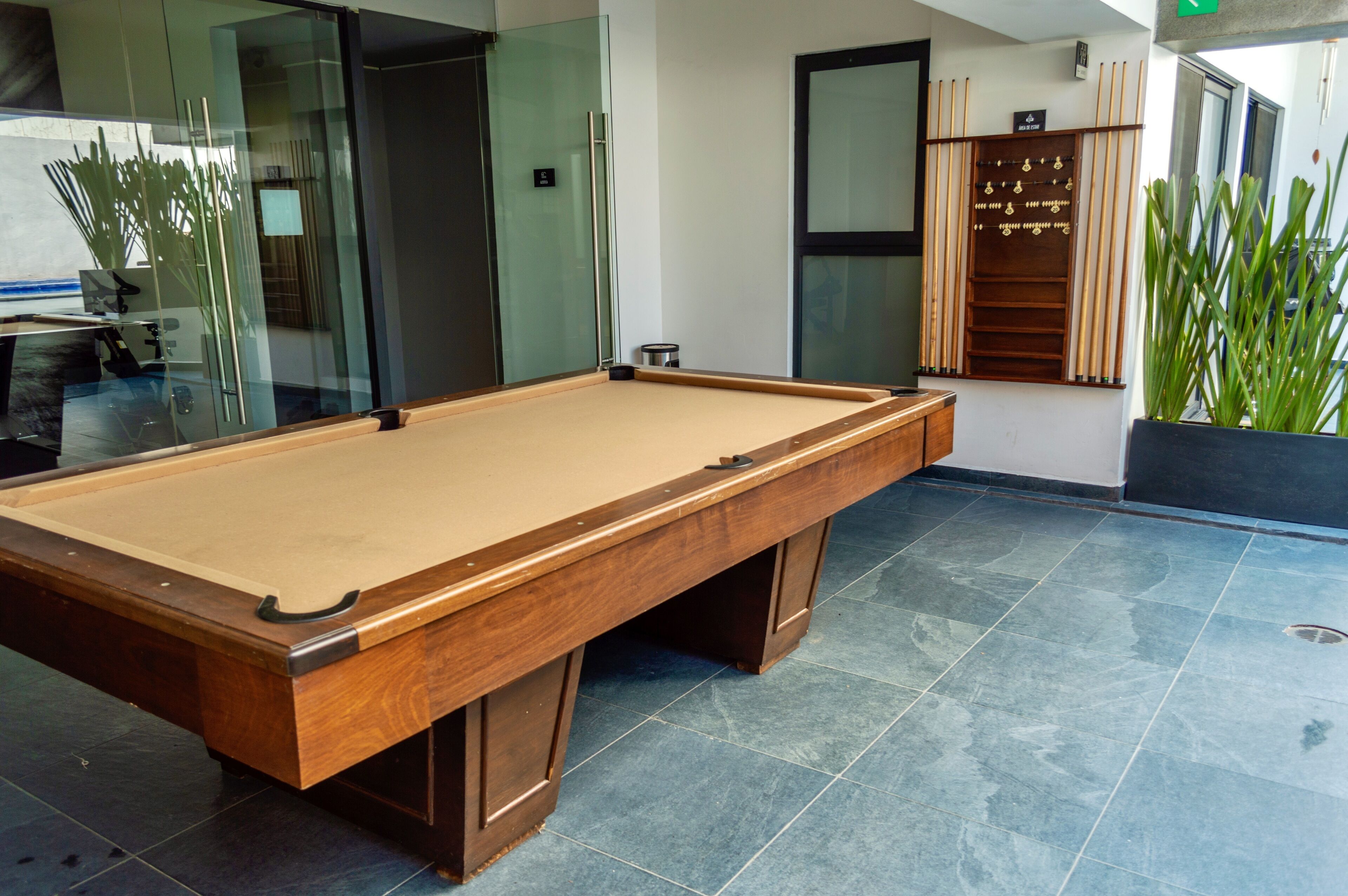 Une table de billard dans une pièce moderne aux murs de verre, avec une plante en pot.