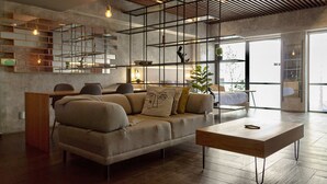 Una sala de estar moderna con un sofá, una mesa de centro y piso de madera. Se observa una escalera con barandilla y una planta en el alféizar.