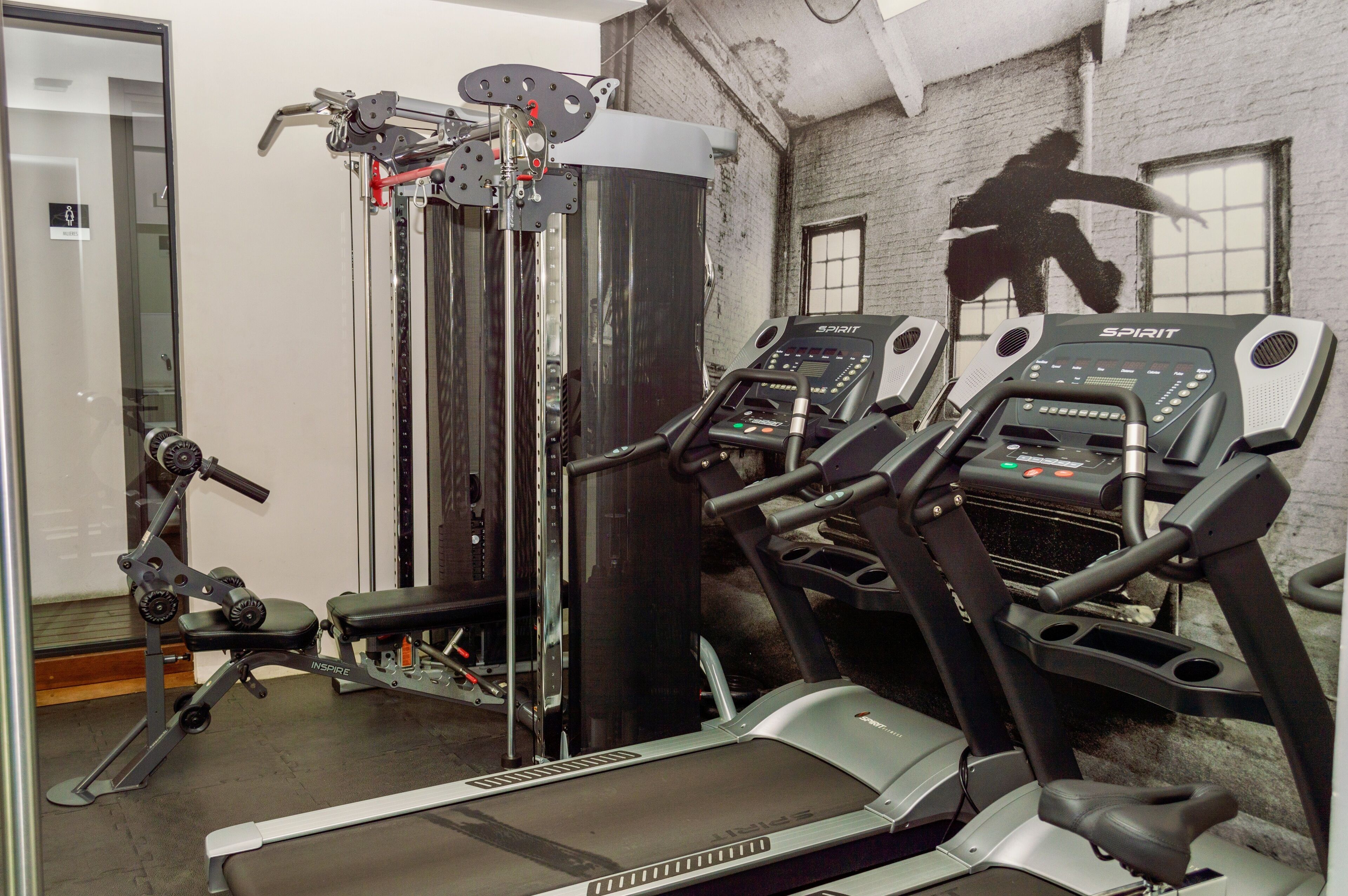 Une salle de sport équipée de tapis de course, d’une machine de musculation et d’un mur orné d’un graffiti représentant une personne.